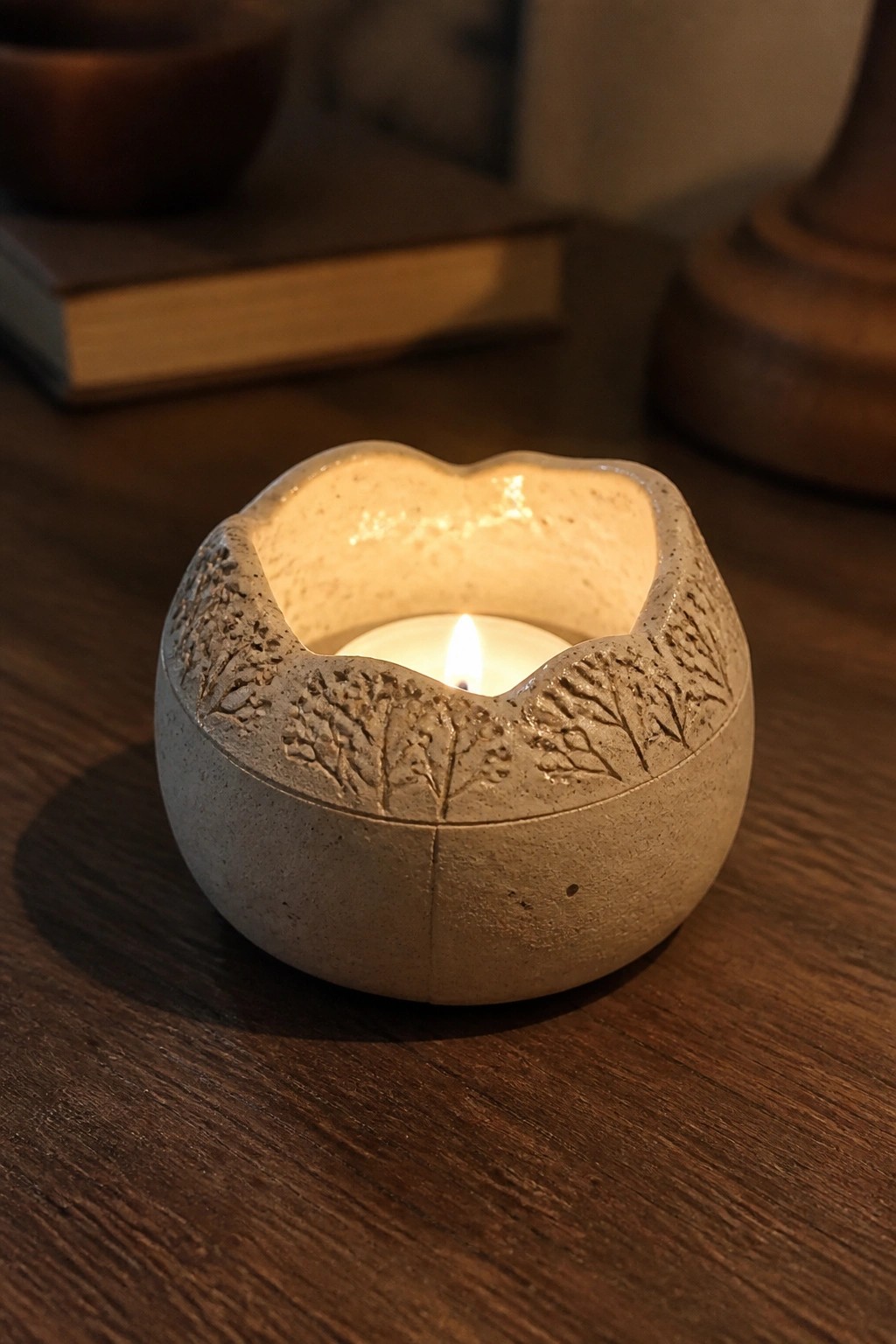 Lit candle in textured ceramic holder with tree etchings on wooden table.