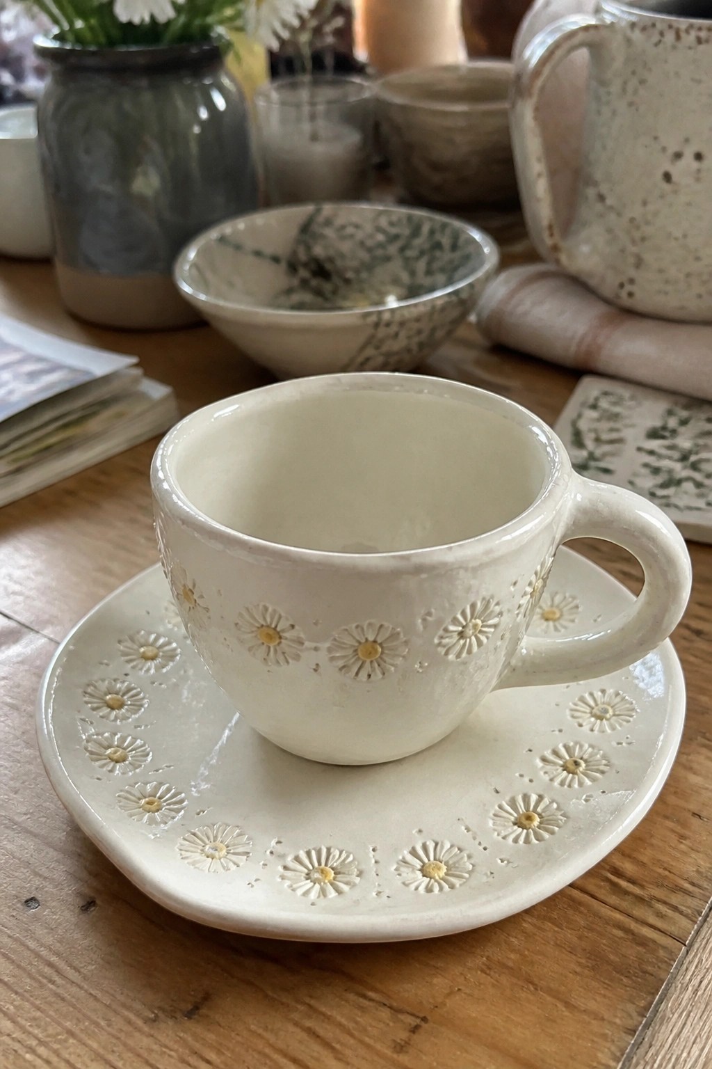 White ceramic cup with embossed daisies on matching saucer atop wooden table