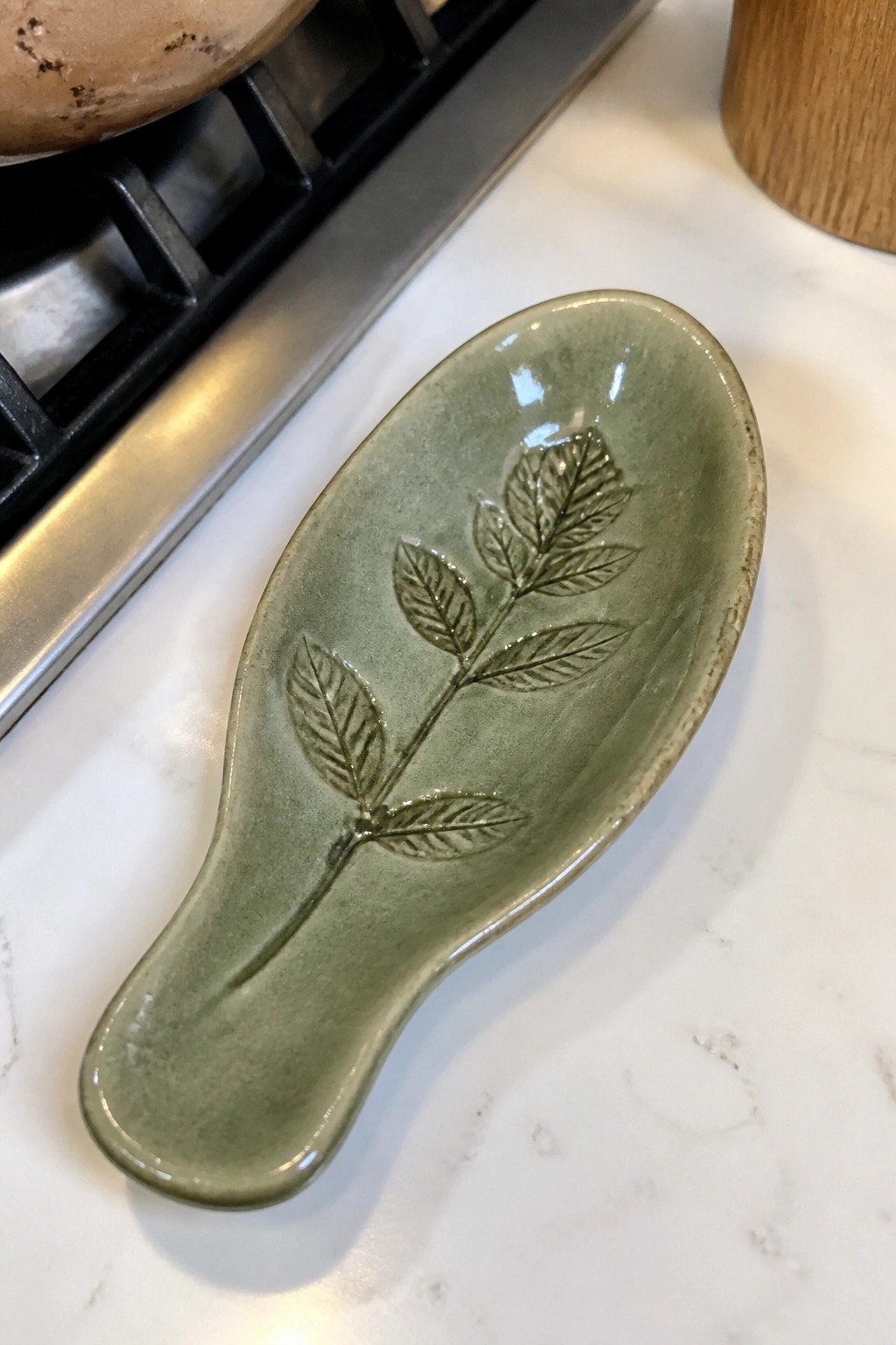 Green ceramic spoon rest with embossed leaf design on white marble counter