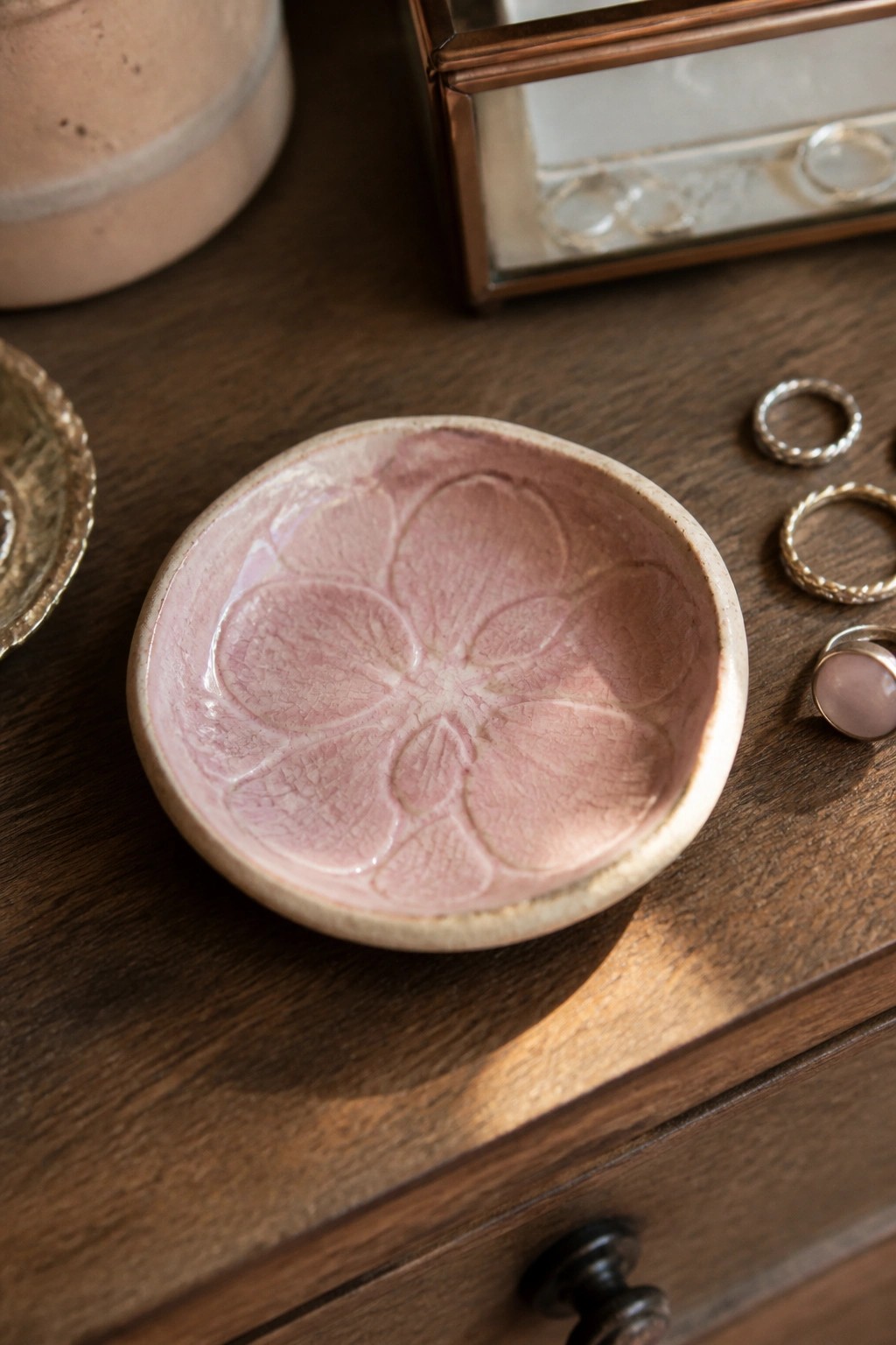 Pink floral ceramic bowl with rings on dark wooden dresser surface