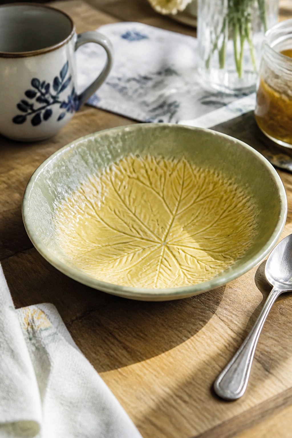 Green ceramic bowl with yellow leaf pattern on wooden table beside spoon