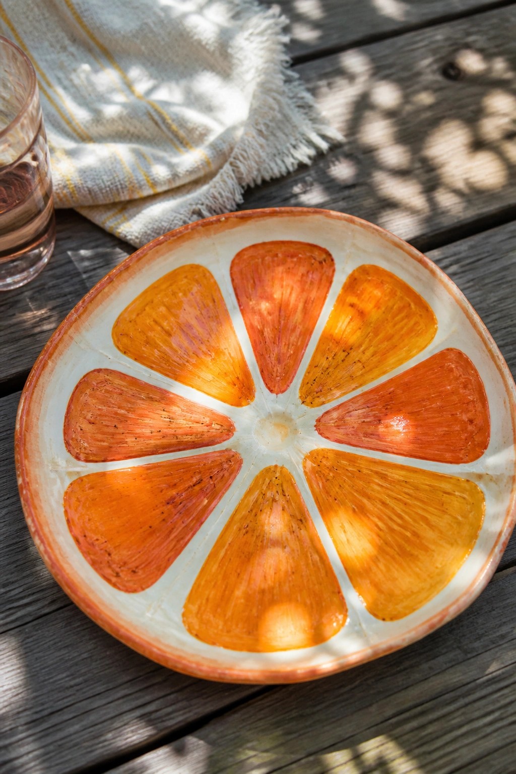 Orange citrus slice ceramic bowl on sunlit wooden table with glass and cloth
