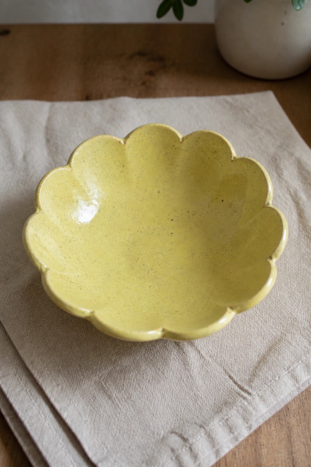 Yellow scalloped ceramic bowl on beige linen atop wooden table