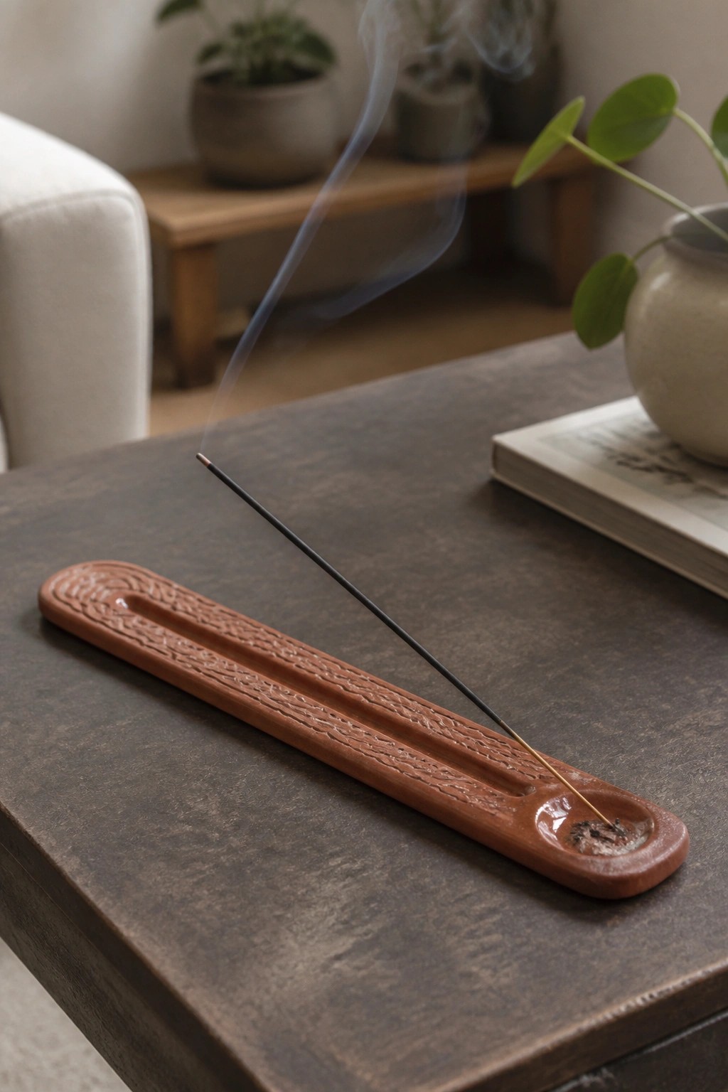 Burning incense stick on ornate terracotta holder with rising smoke on wooden table