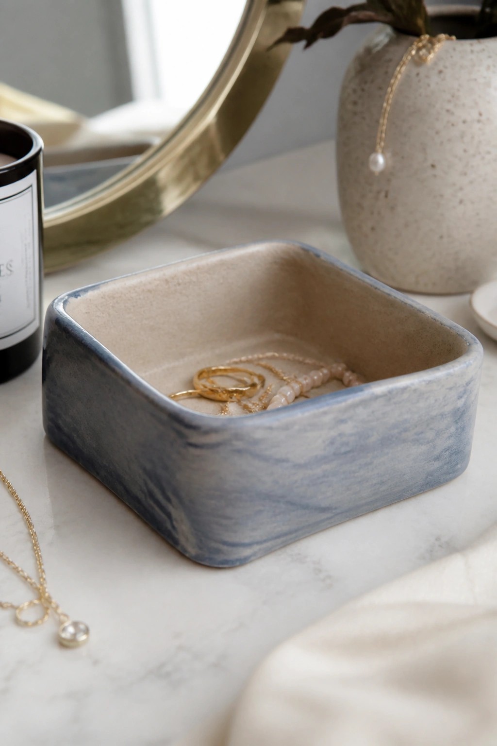 Blue marbled ceramic tray holding gold rings and pink beaded necklace on marble