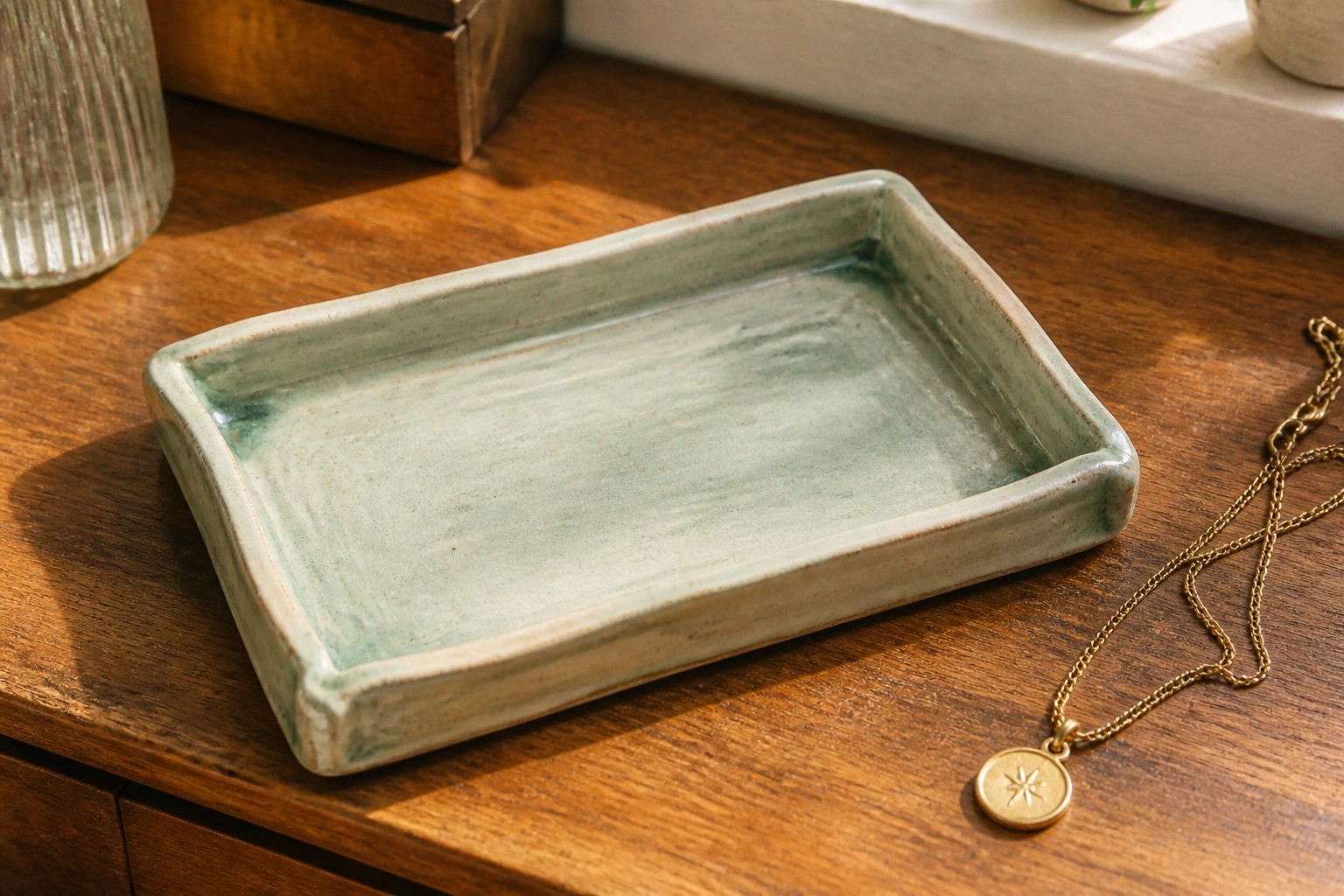 Square green ceramic tray on wooden dresser beside gold leaf necklace