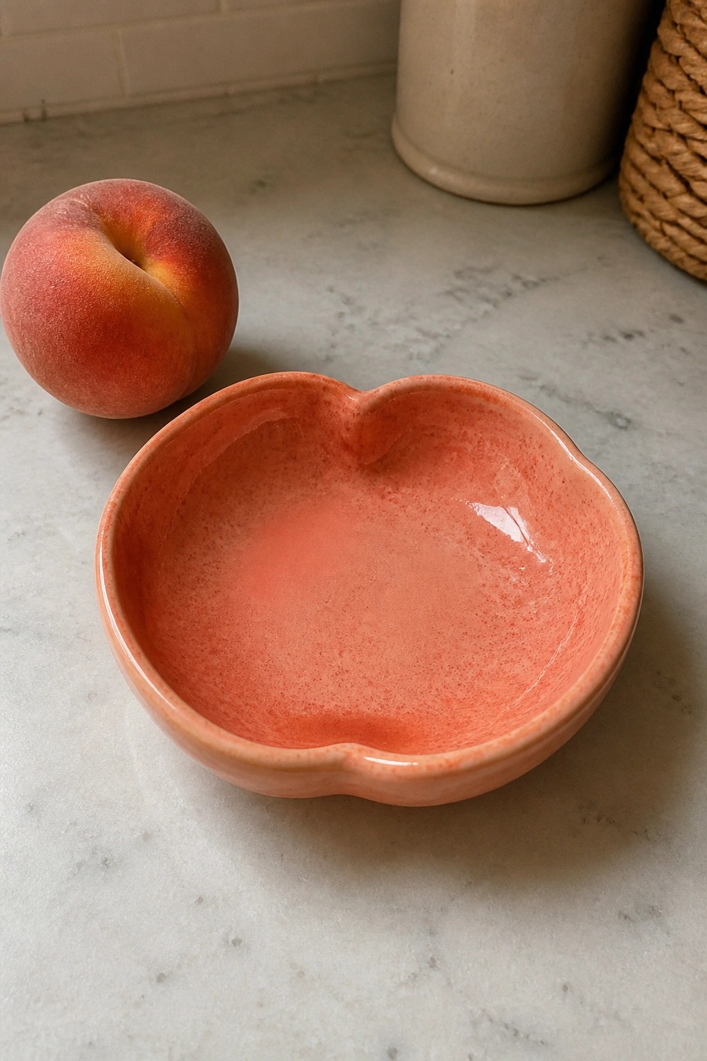 Peach beside pink ceramic peach-shaped bowl on marble countertop