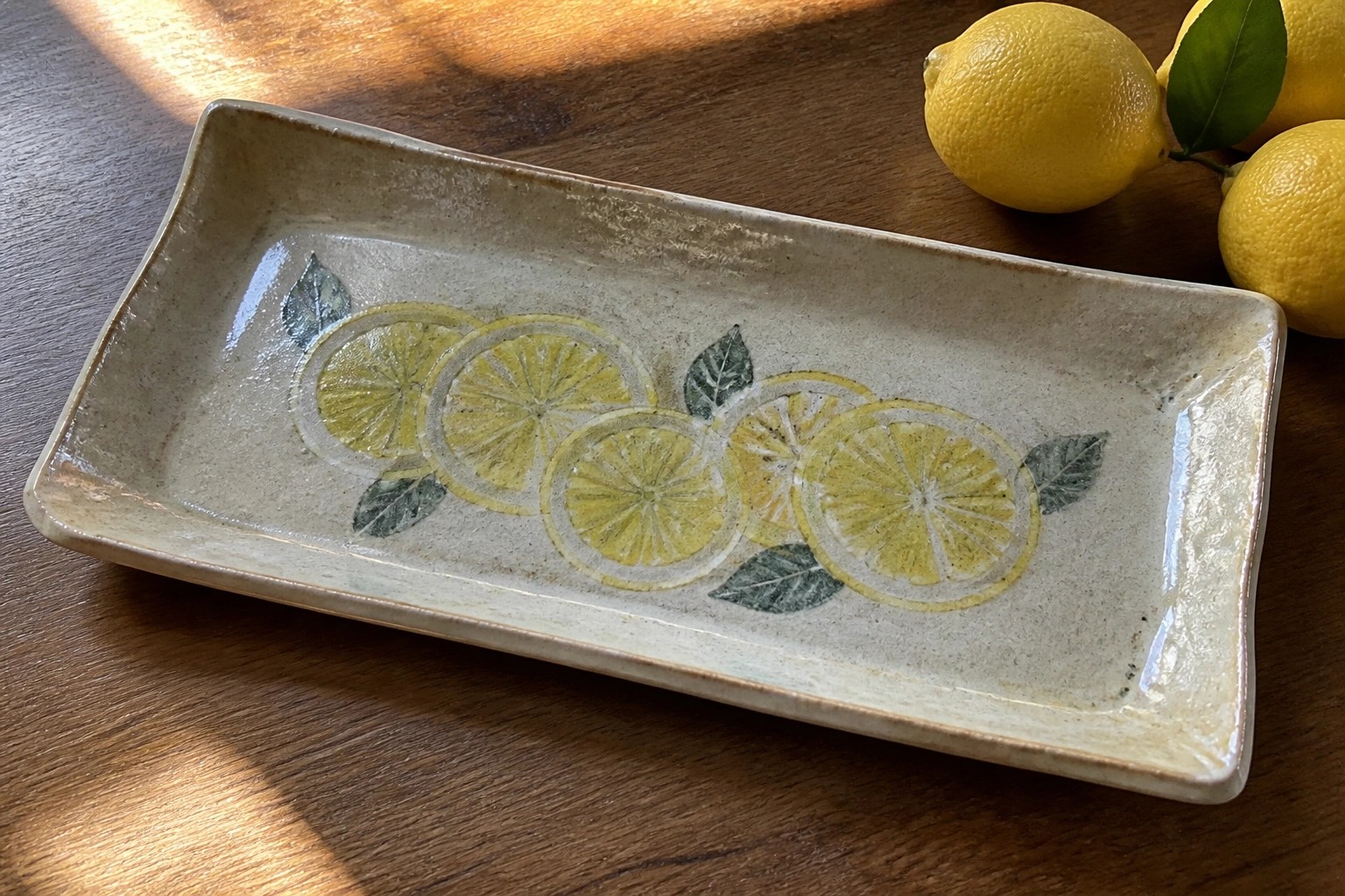 Speckled ceramic platter with lemon slices and leaves on wooden table