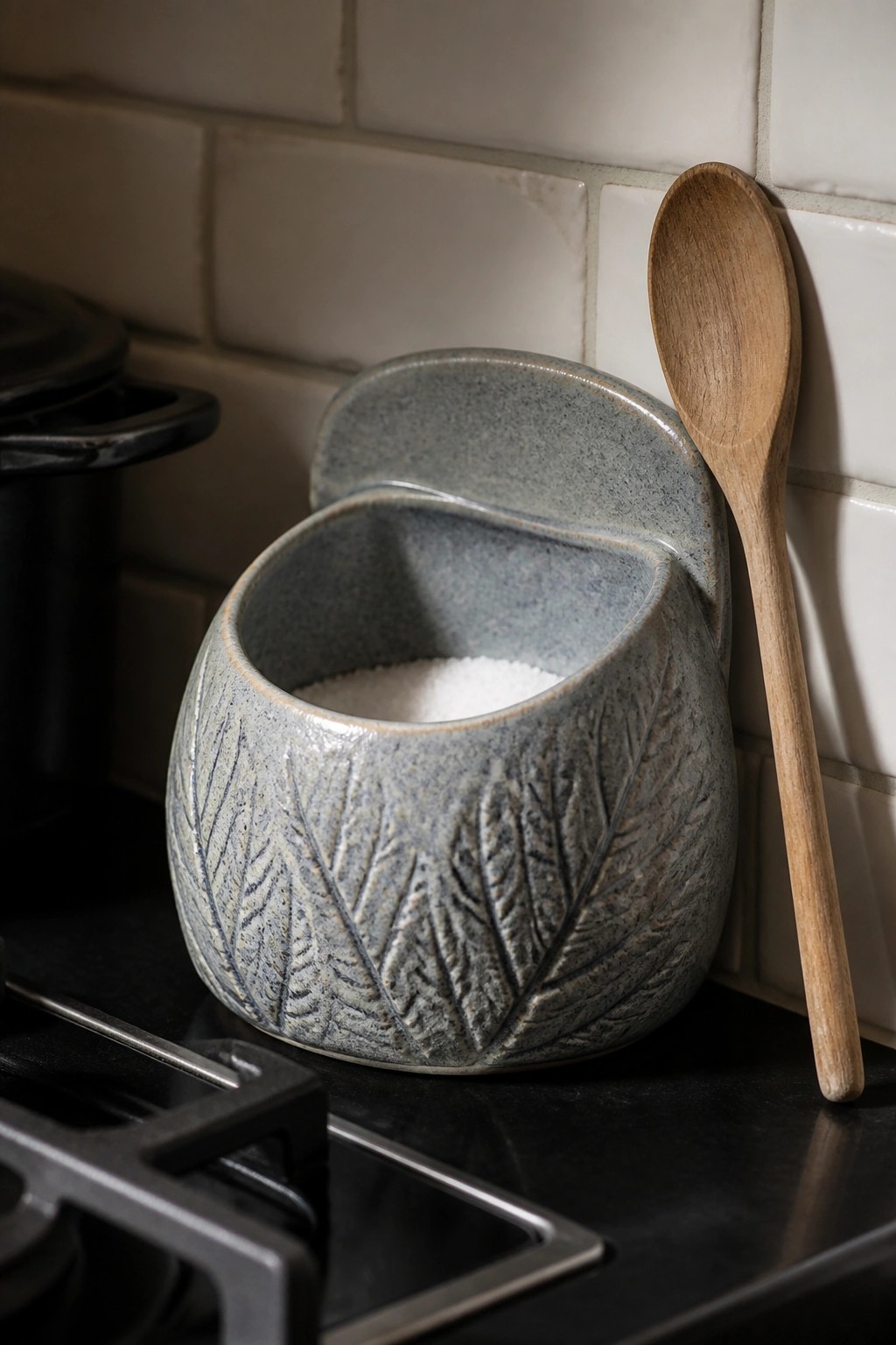 Gray ceramic bowl with leaf pattern holding salt beside wooden spoon on stove