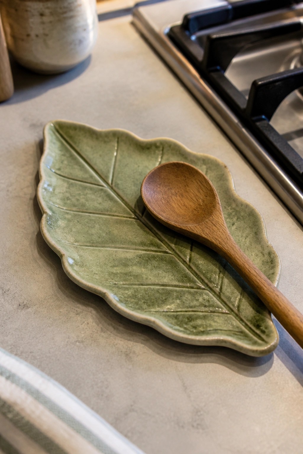 Green ceramic leaf-shaped dish with wooden spoon on kitchen countertop