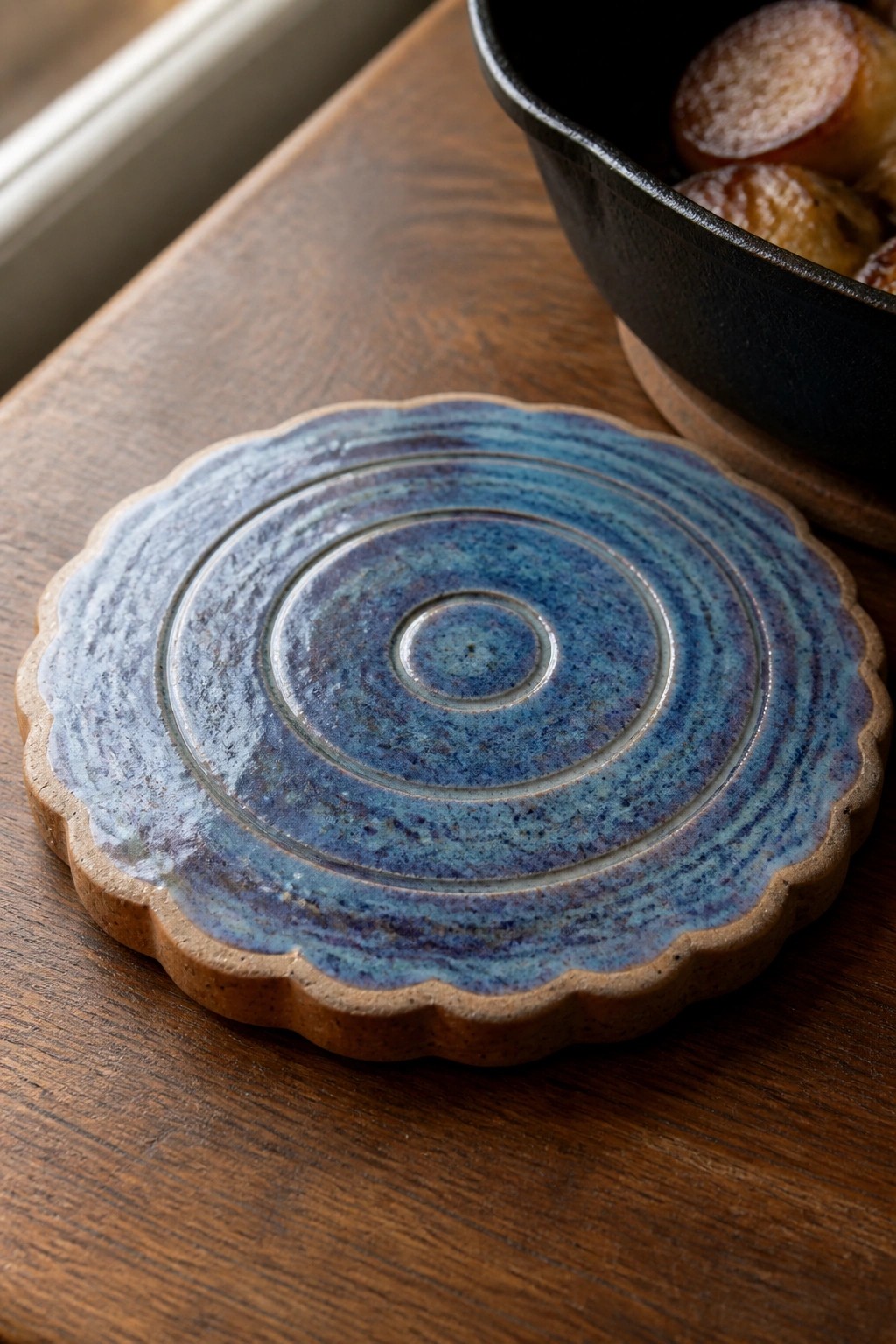 Blue ceramic trivet with concentric rings and scalloped edge on wood table