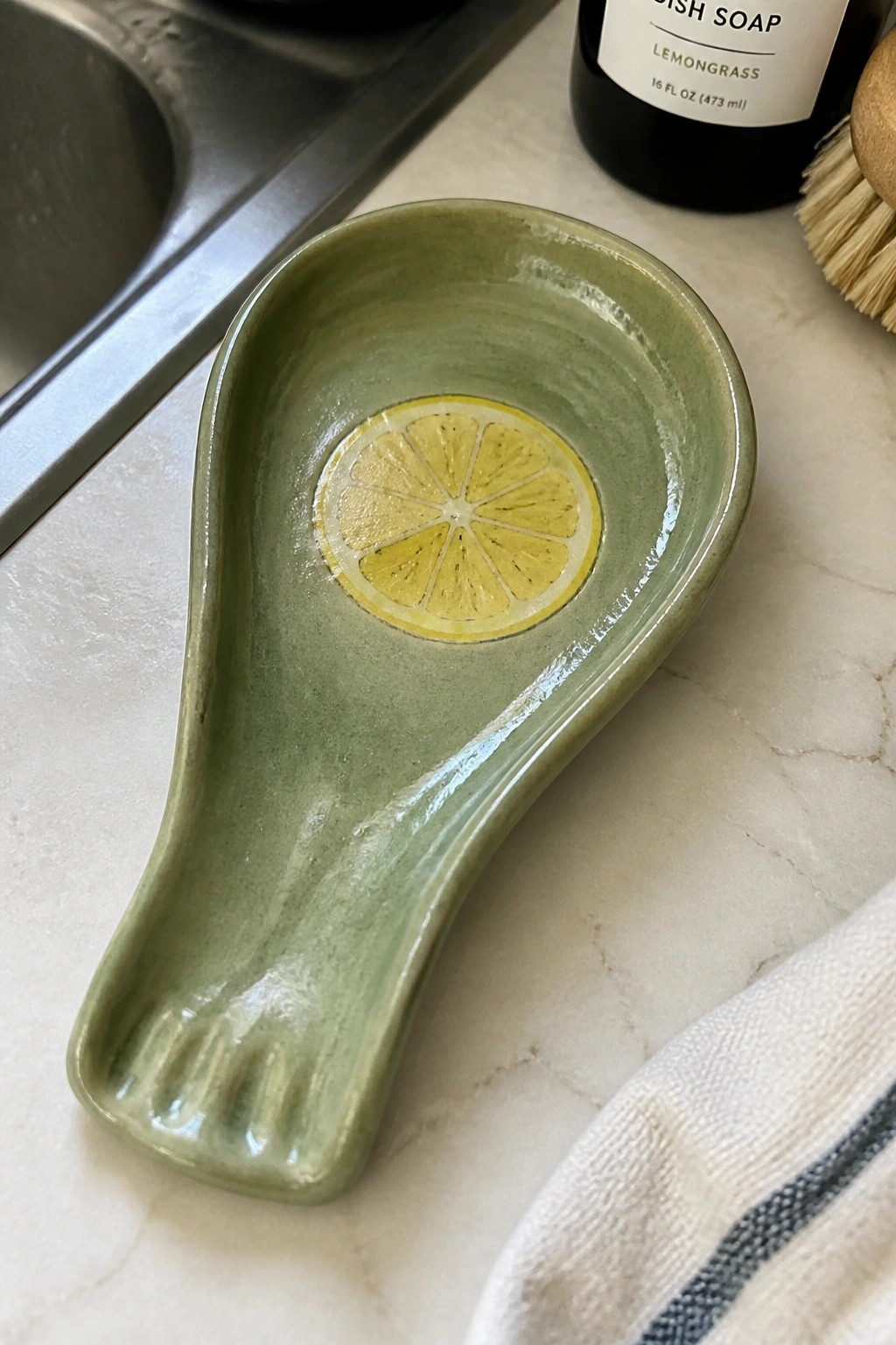 Green ceramic spoon rest with lemon slice on marble kitchen counter