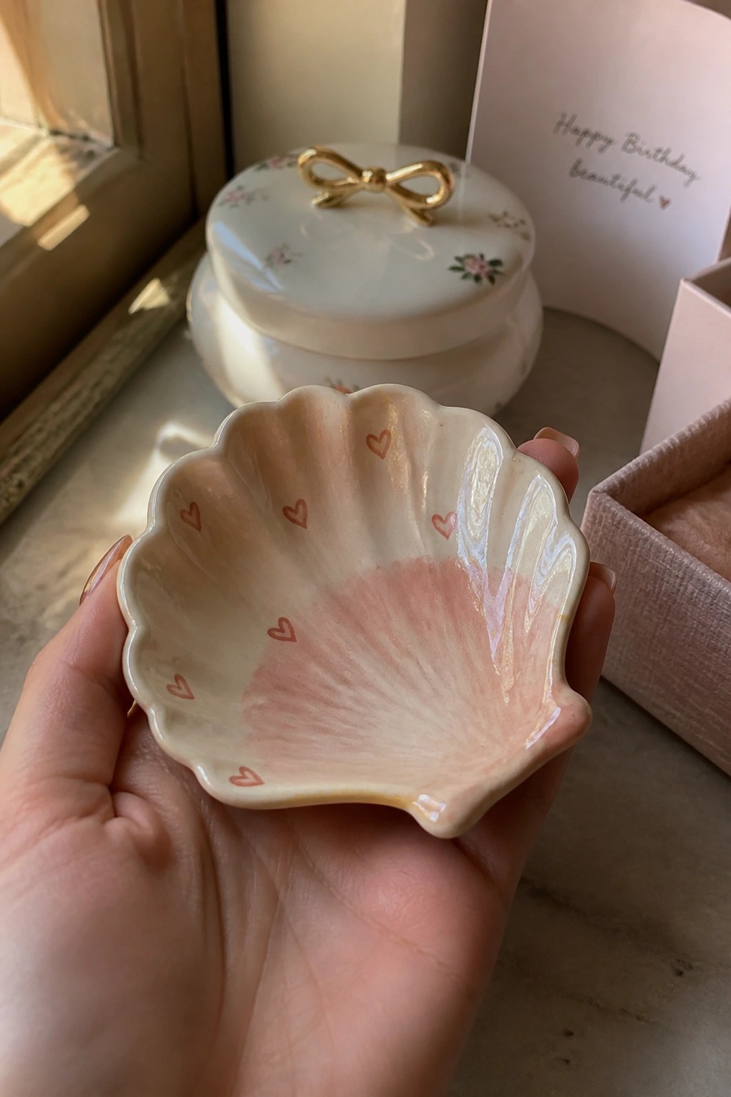 Hand holding scallop-shell ceramic dish with pink gradient and red hearts.