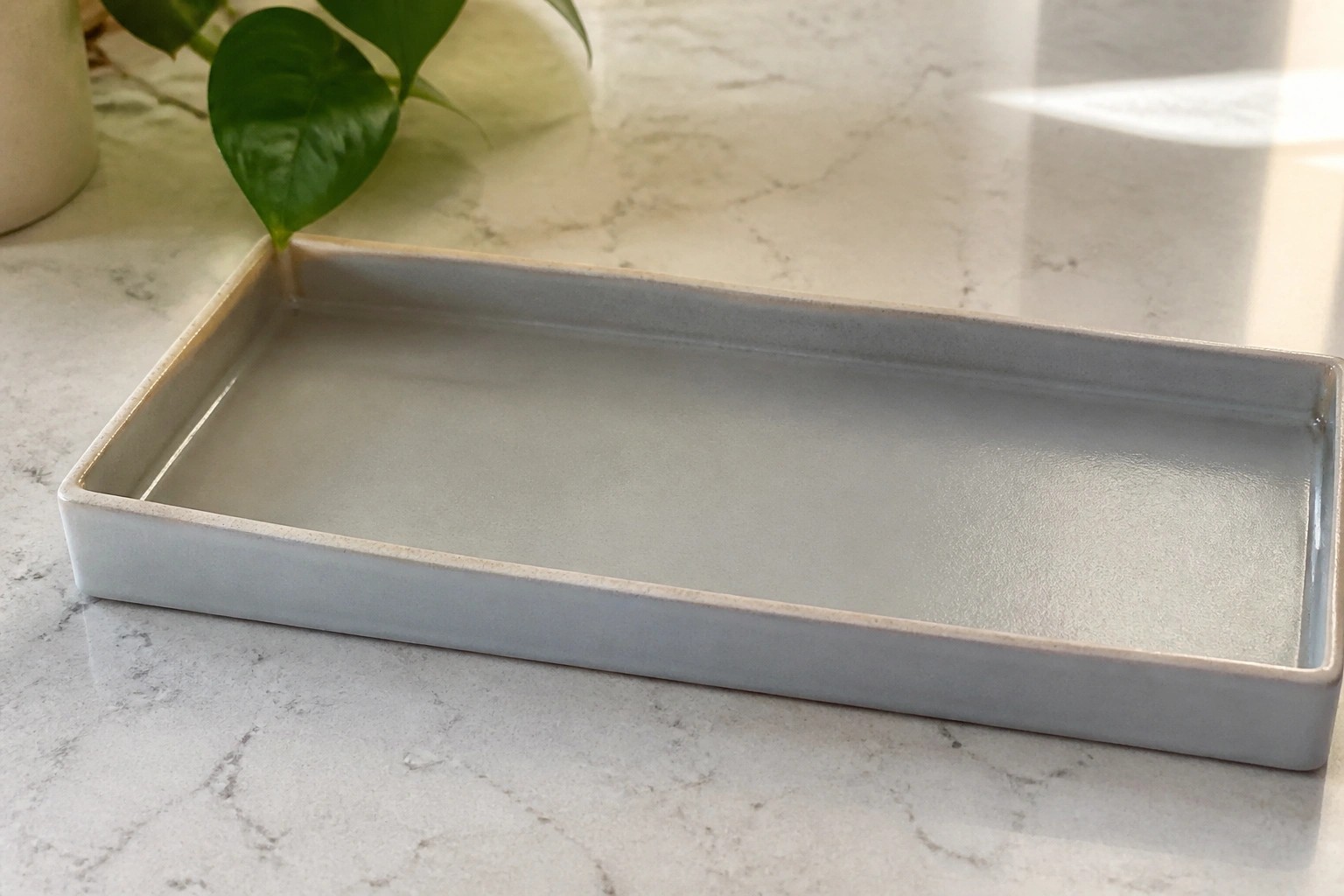 Gray square ceramic tray on marble countertop with monstera leaf by sunny window