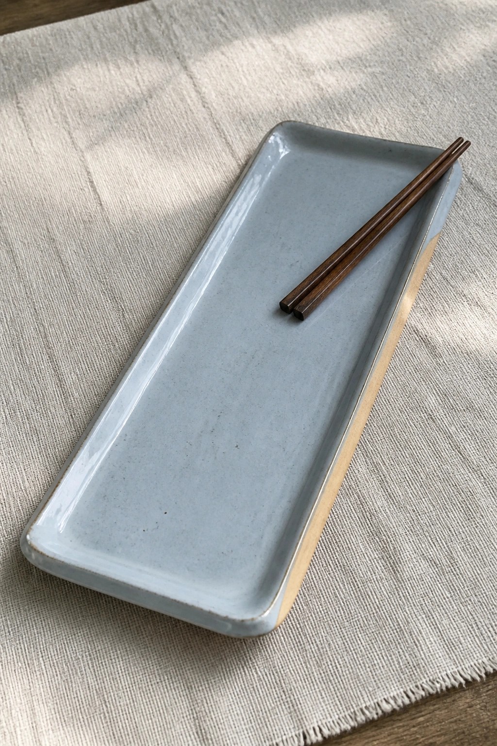 Light blue rectangular ceramic plate with wooden chopsticks on beige linen cloth