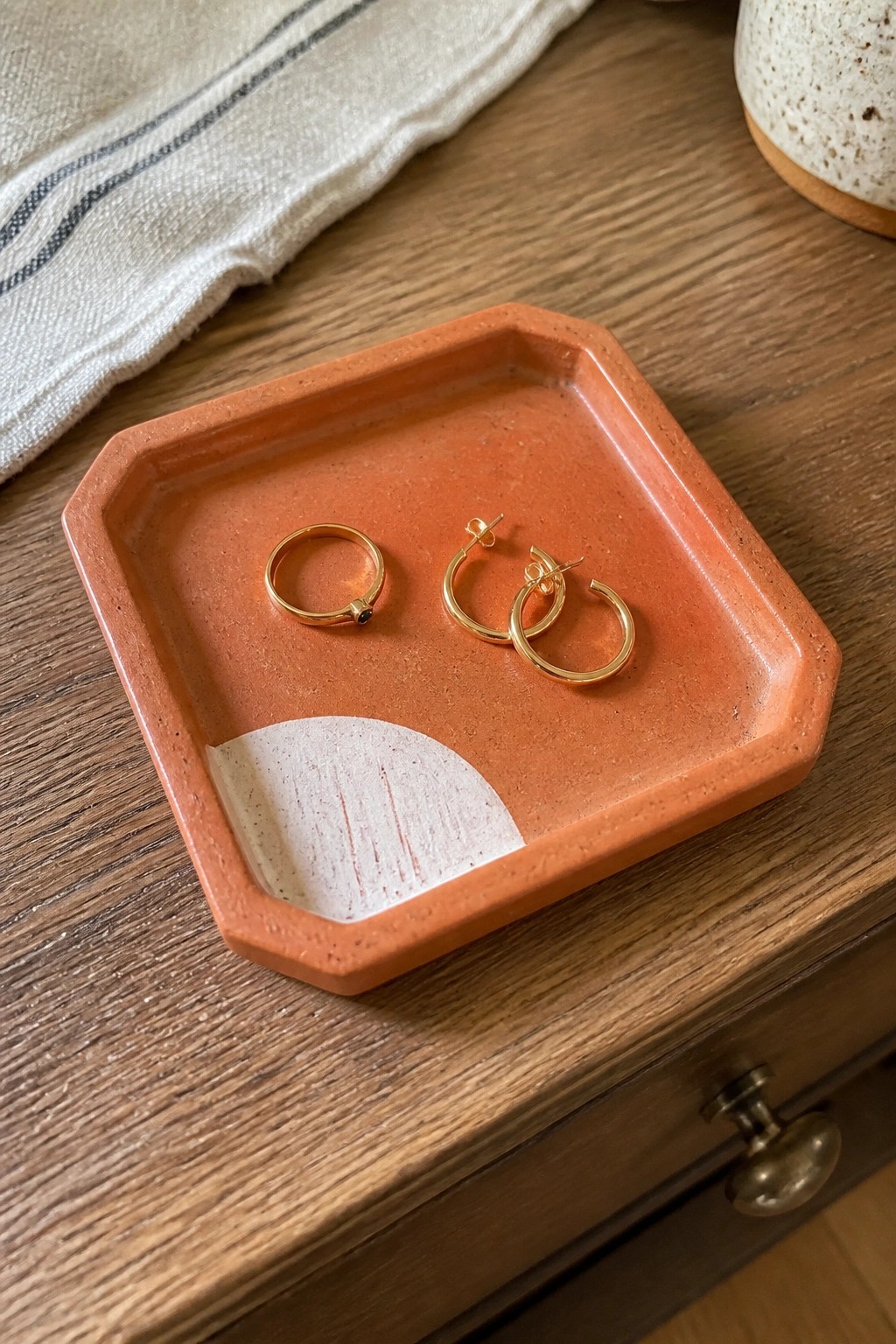 Gold hoop earrings and ring in orange ceramic tray on wooden dresser