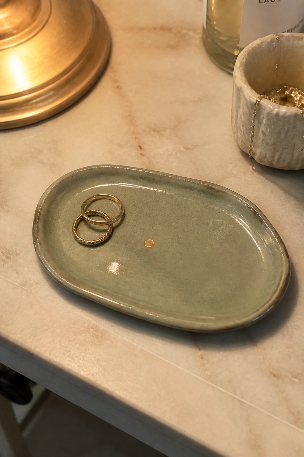 Green ceramic tray with two gold rings on marble countertop