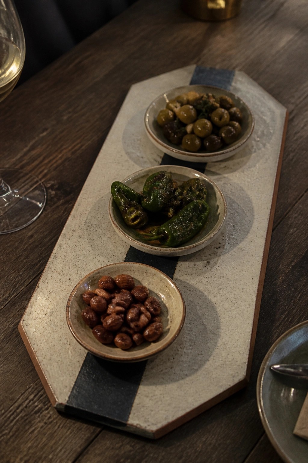 Three ceramic bowls of olives, peppers, and nuts on a striped platter.