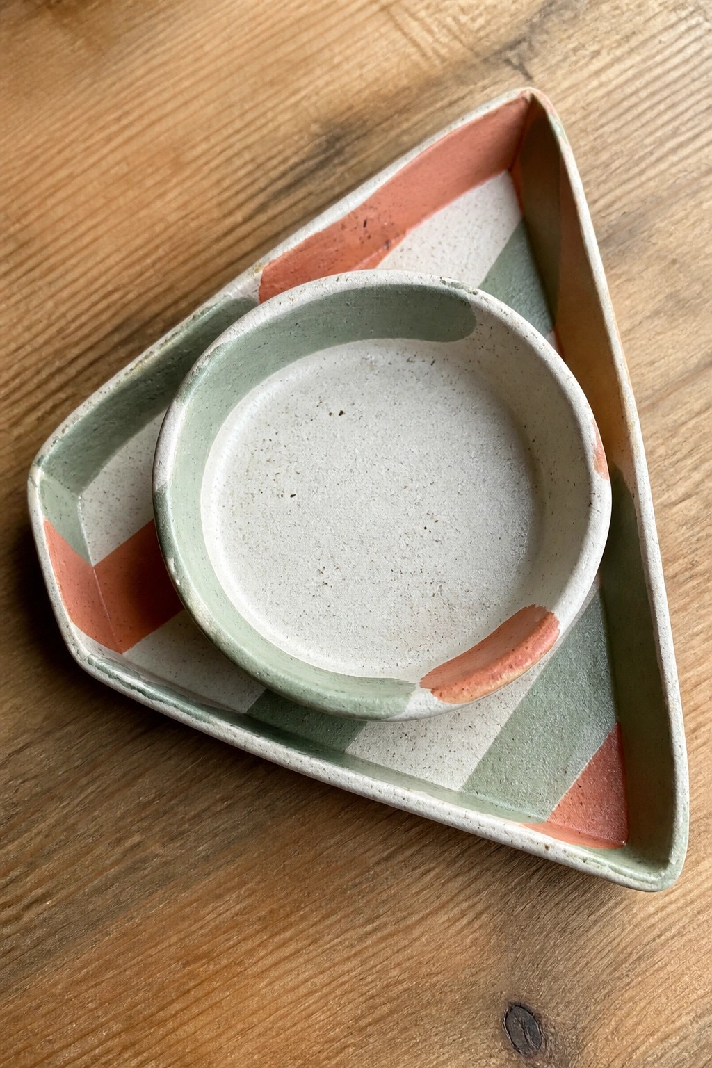 Round speckled bowl in striped triangular ceramic tray on wooden table