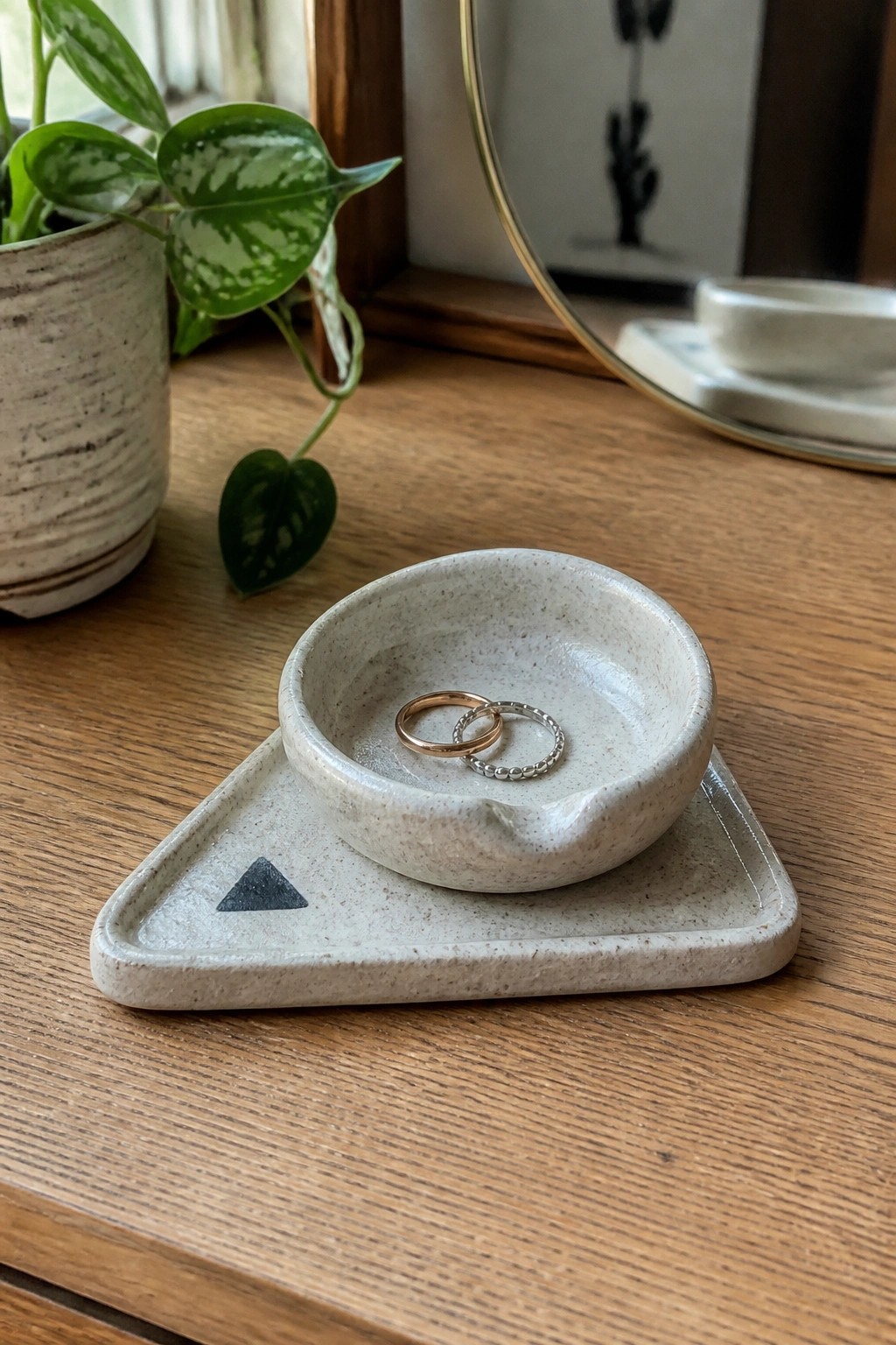 Two rings in speckled ceramic bowl on triangular tray atop wood.