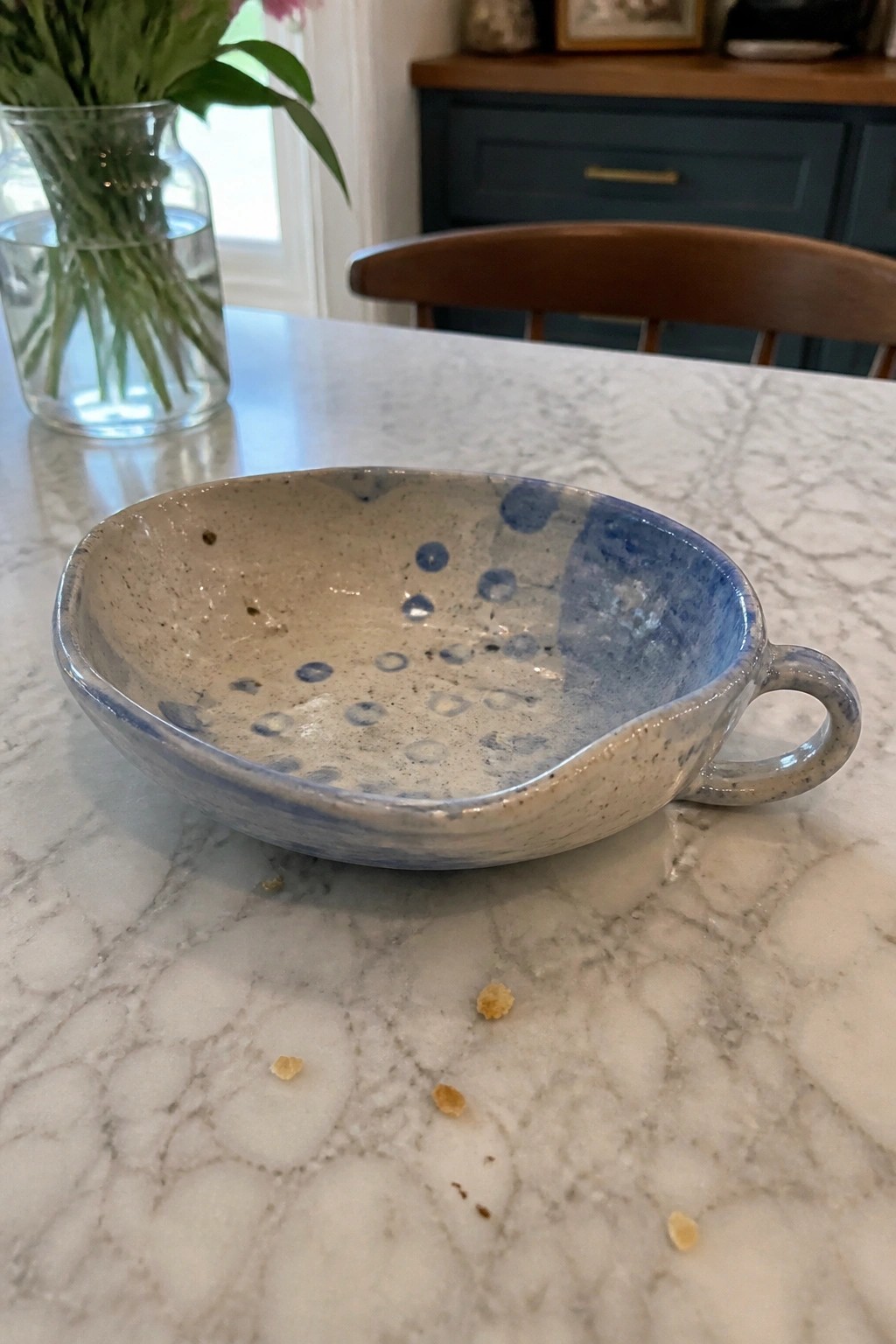 Blue-speckled ceramic bowl with handle on marble countertop beside crumbs