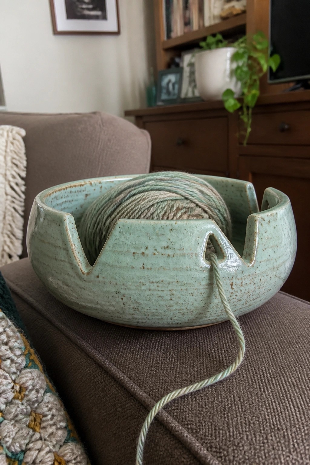 Light green ceramic yarn bowl with green yarn ball on brown couch