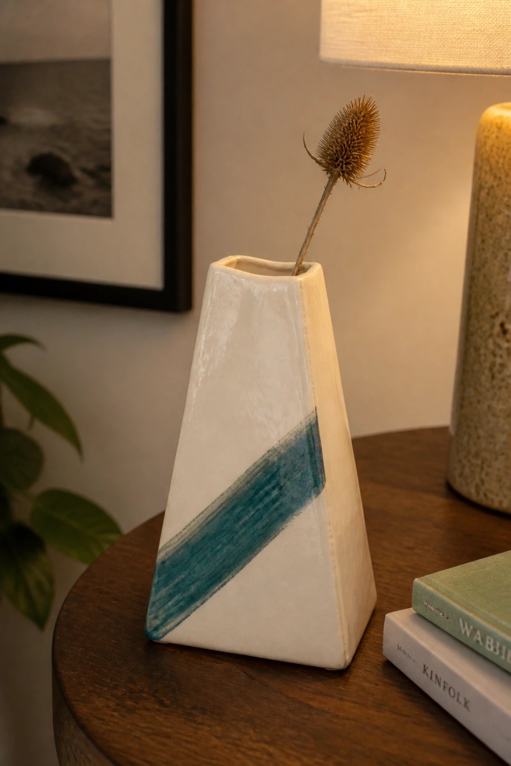 White triangular vase with teal stripe holding dried thistle on wooden table