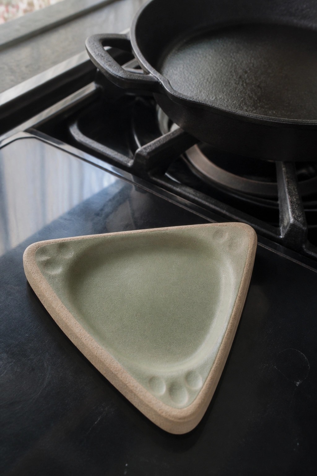 Triangular green ceramic dish with cat paw prints beside black cast iron skillet