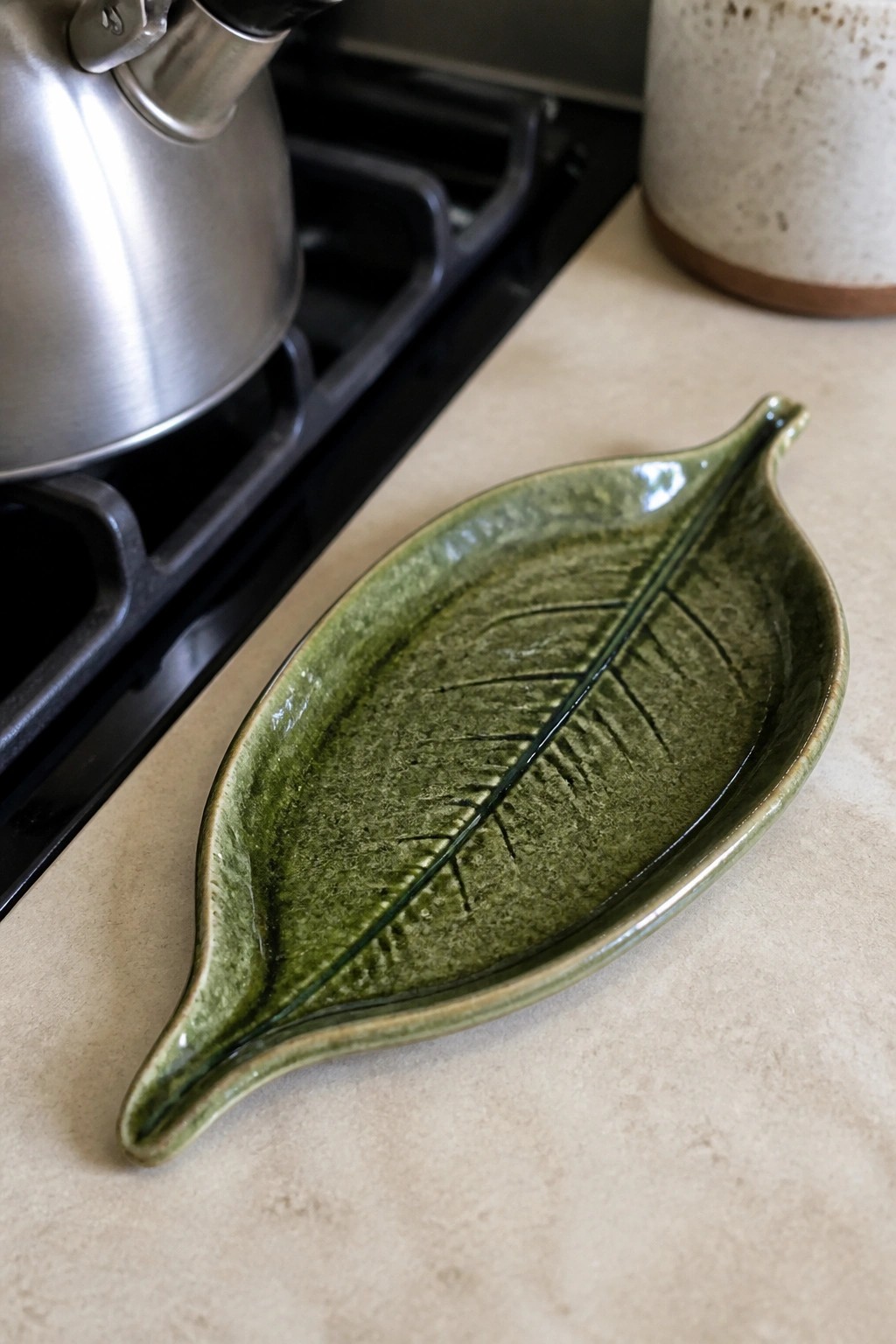 Green glazed ceramic leaf-shaped dish on kitchen countertop near stovetop and kettle