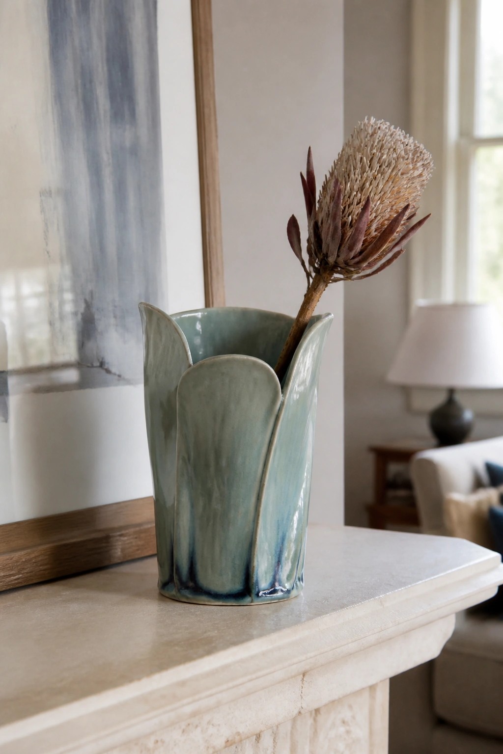 Teal ceramic vase with scalloped rim holding dried flower on marble mantel