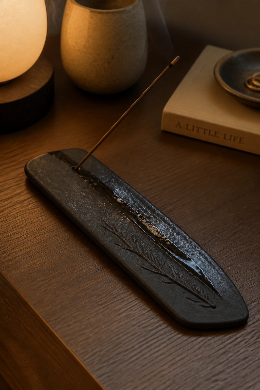 Burning incense in dark ceramic holder with feather design on wooden table