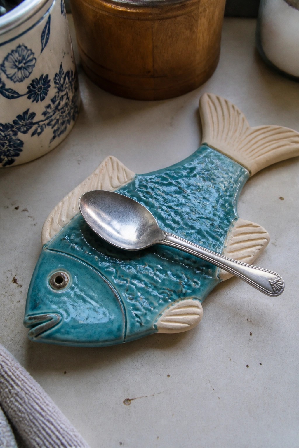 Silver spoon on turquoise fish-shaped ceramic spoon rest with beige fins