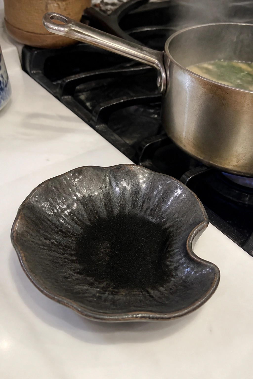 Black ceramic bowl on white counter near soup pot on lit gas stove
