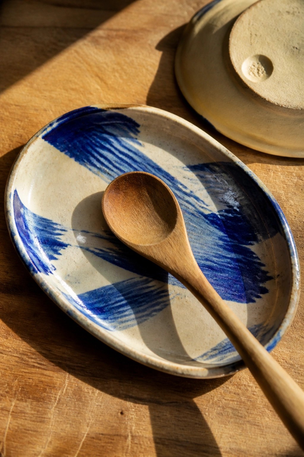 Blue brushstroke ceramic plate with wooden spoon on sunlit wooden table