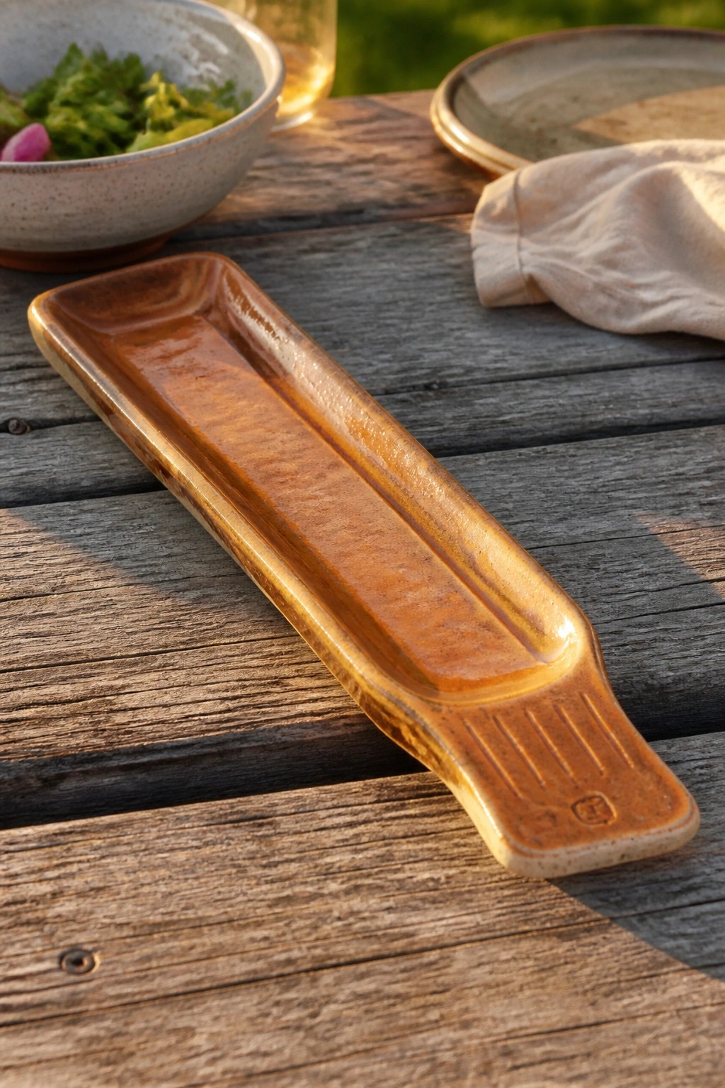 Glossy brown ceramic tray on rustic wooden table beside salad bowl and napkin.