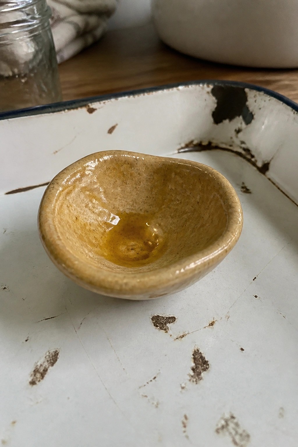 Small speckled ceramic bowl with oil in chipped white enamel tray on wood