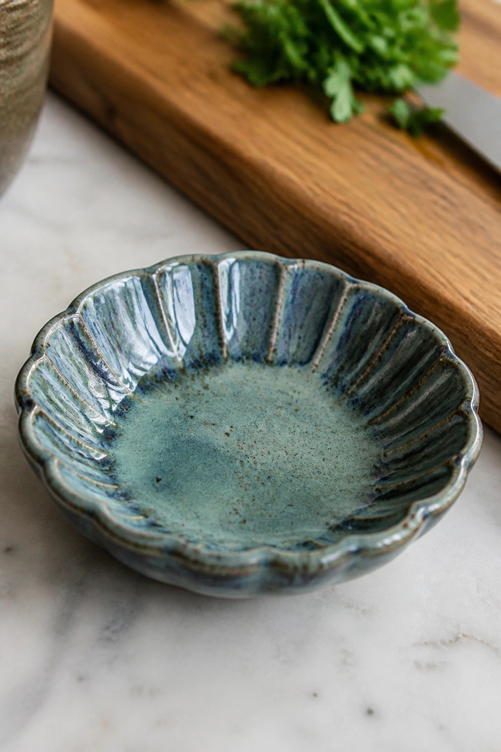 Blue ceramic bowl with scalloped edges on marble beside wooden board and herbs.