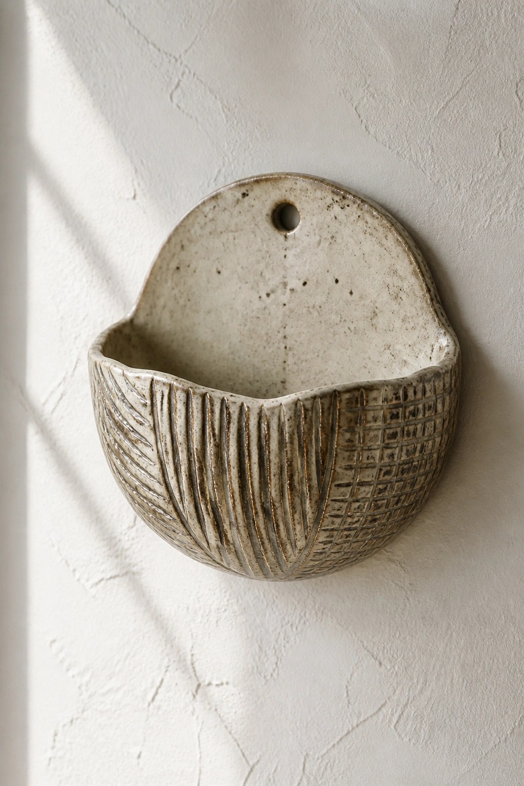 Speckled ceramic wall pocket with leaf and grid patterns on white wall