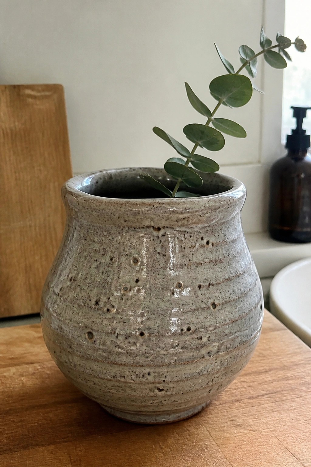 Speckled ceramic vase holding eucalyptus branch on wooden kitchen counter.