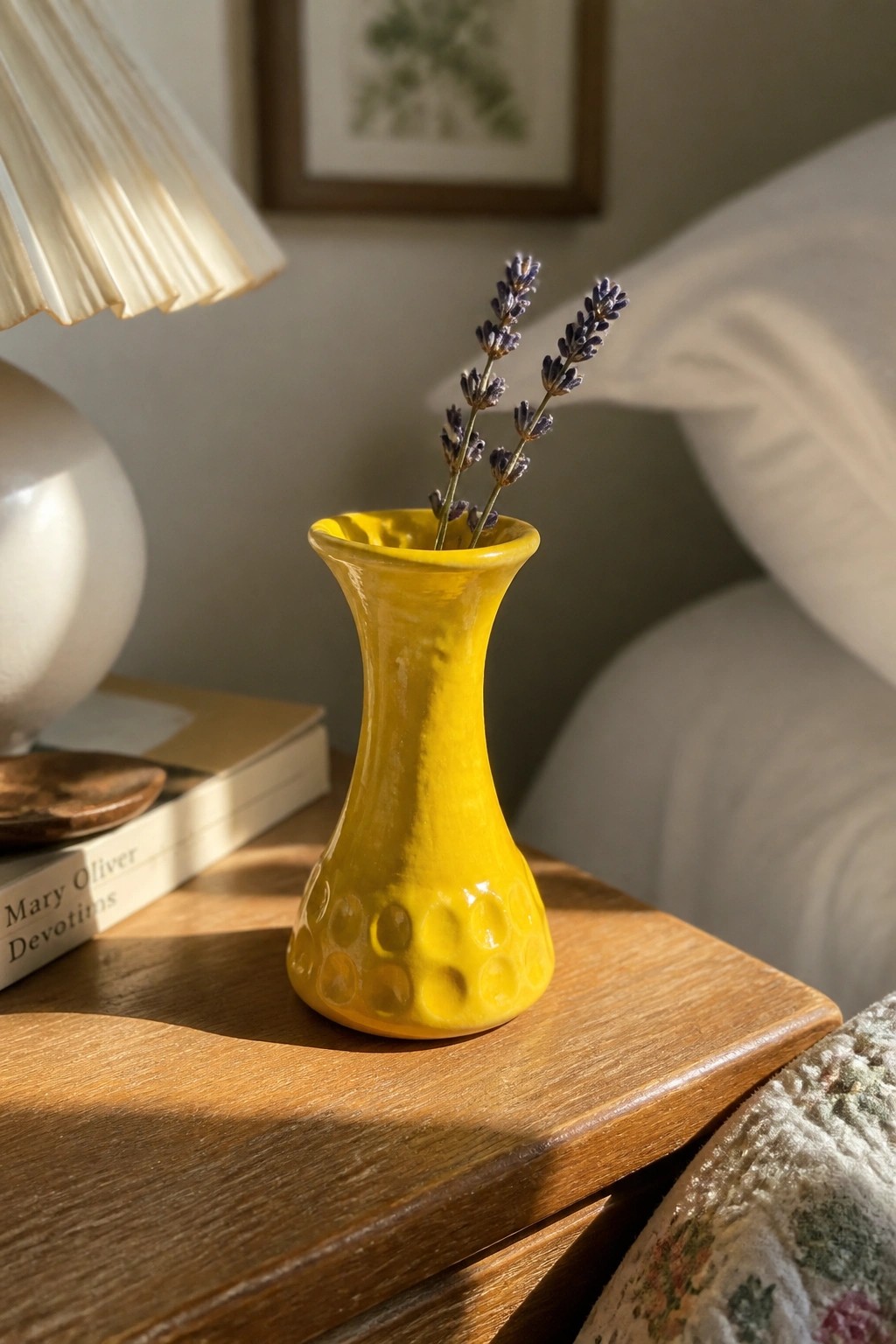 Yellow ceramic vase with lavender on sunlit wooden nightstand beside books and lamp