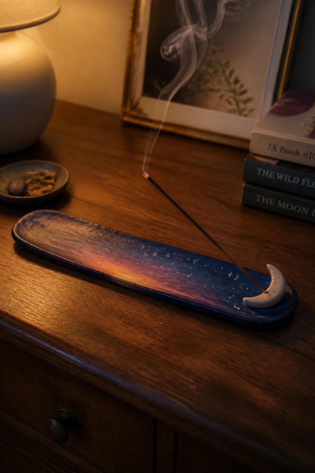 Incense smoke curls from a starry blue-orange ceramic holder with crescent moon on wood.