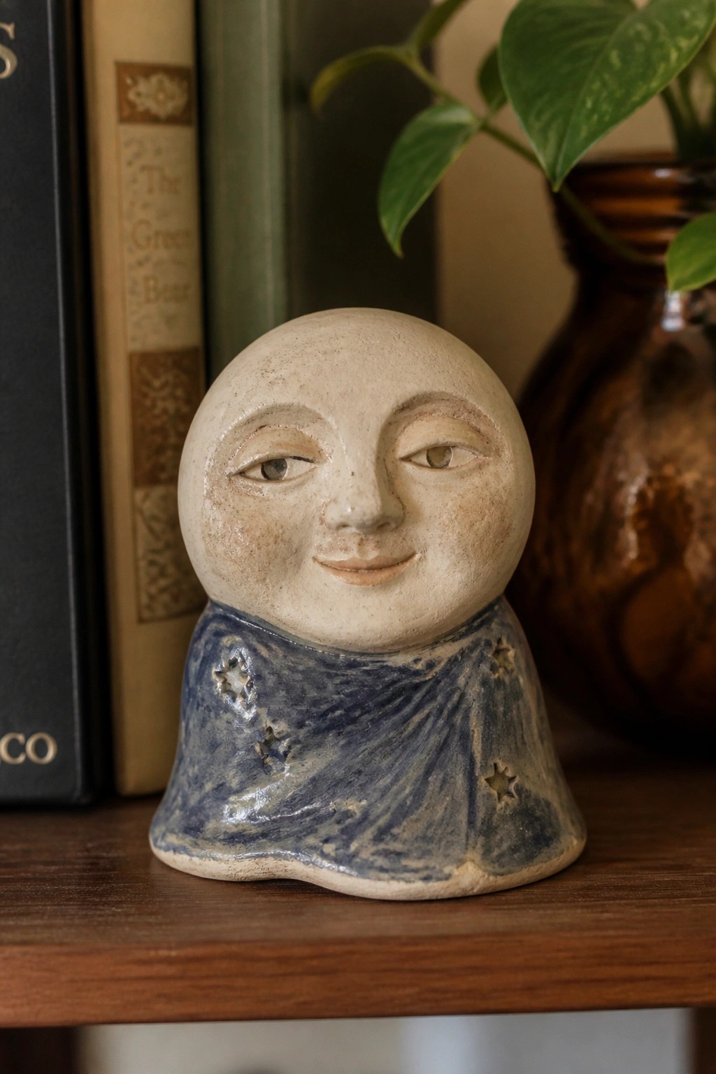 Ceramic smiling moon face with blue starry cloak on wooden shelf