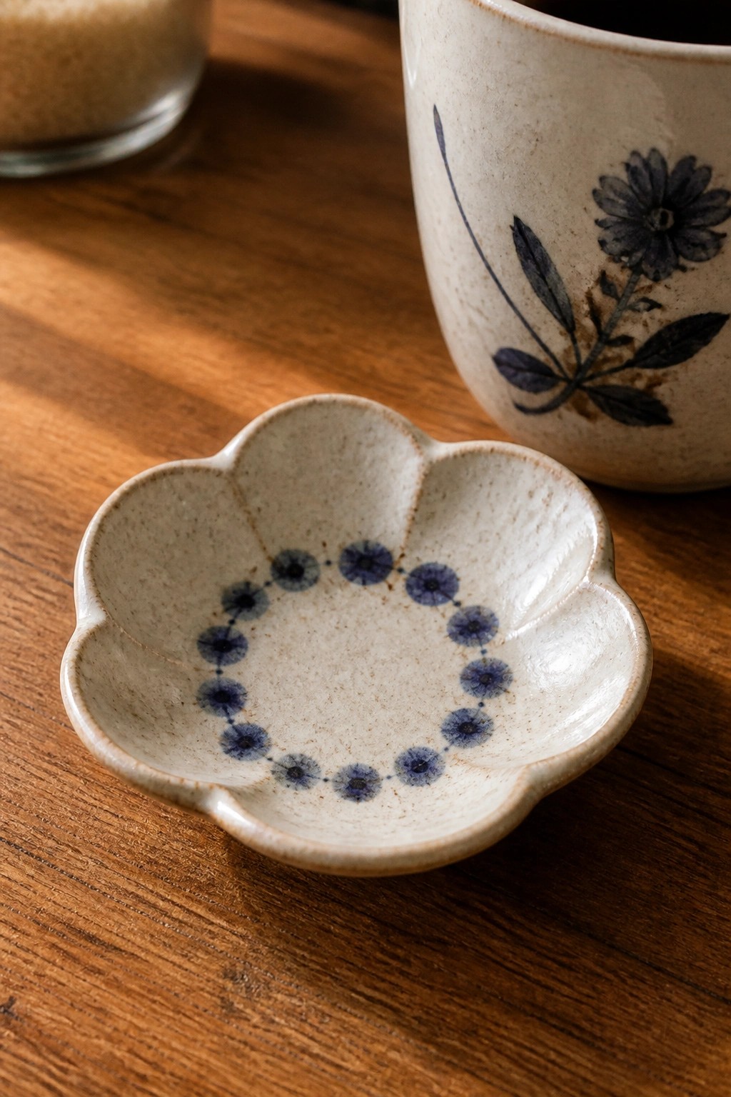 Small scalloped ceramic dish with blue dots beside floral mug on wood table