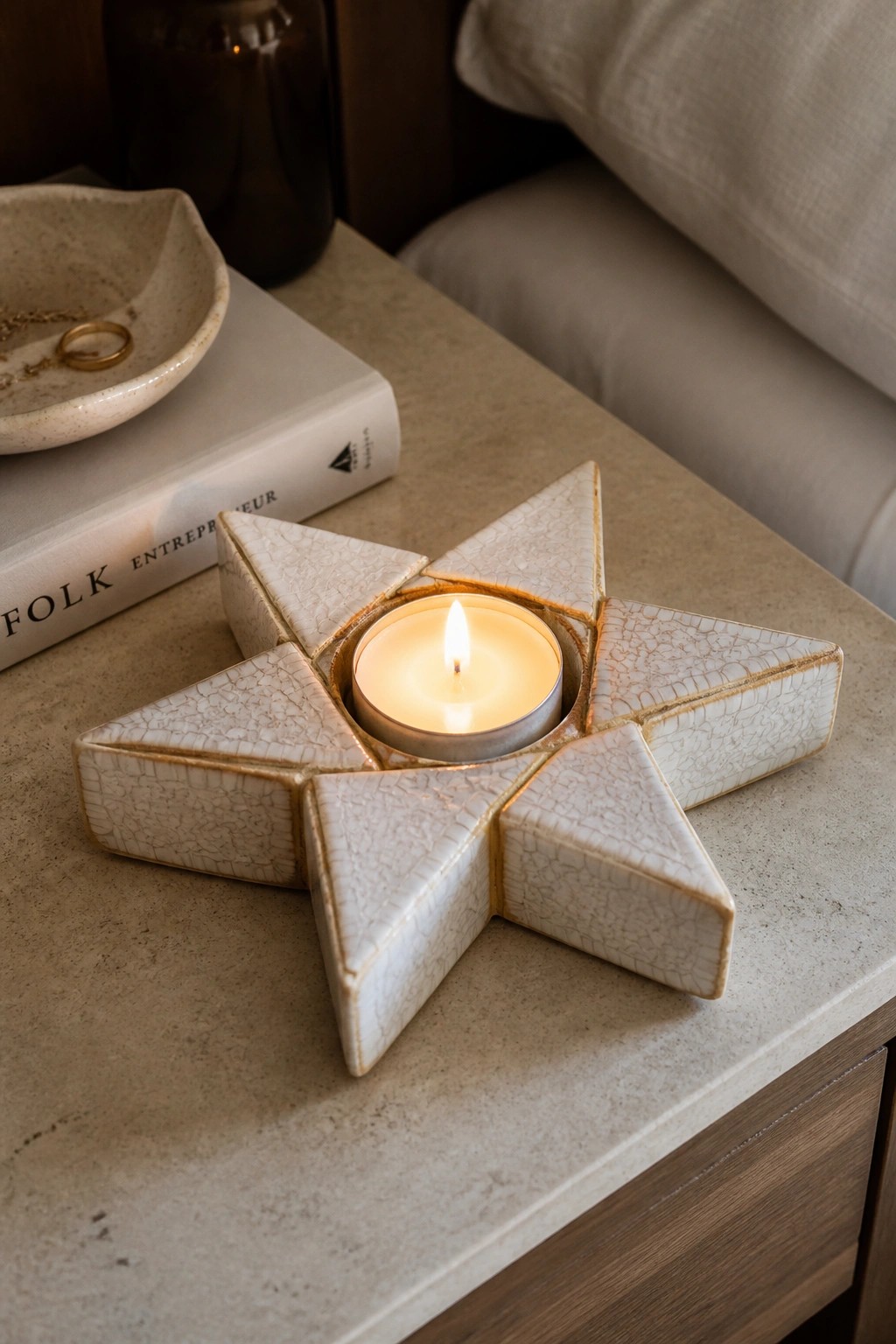 Lit candle in crackle-glazed white star-shaped ceramic holder on marble table