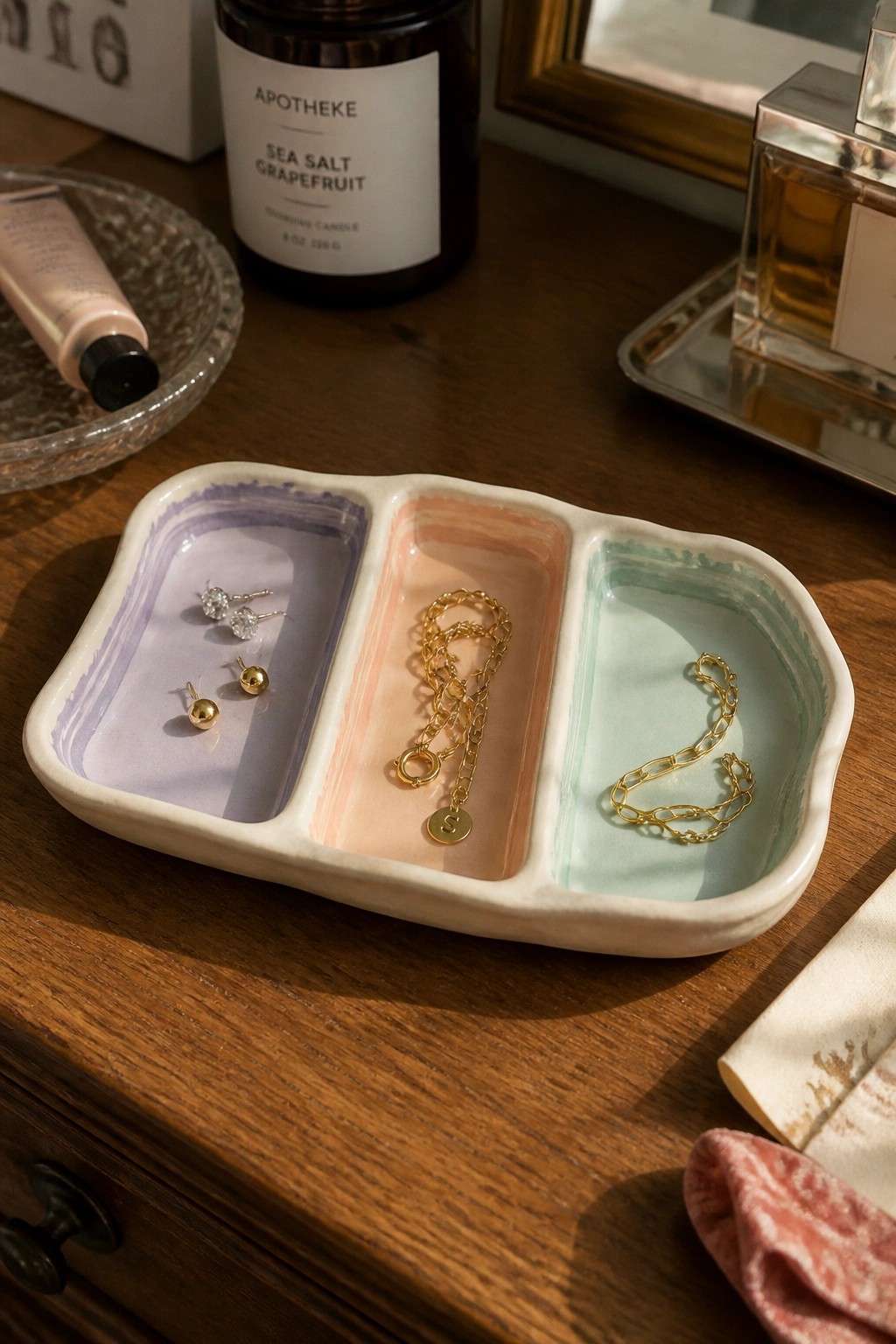 Pastel three-section ceramic tray holding gold earrings and necklaces on wood