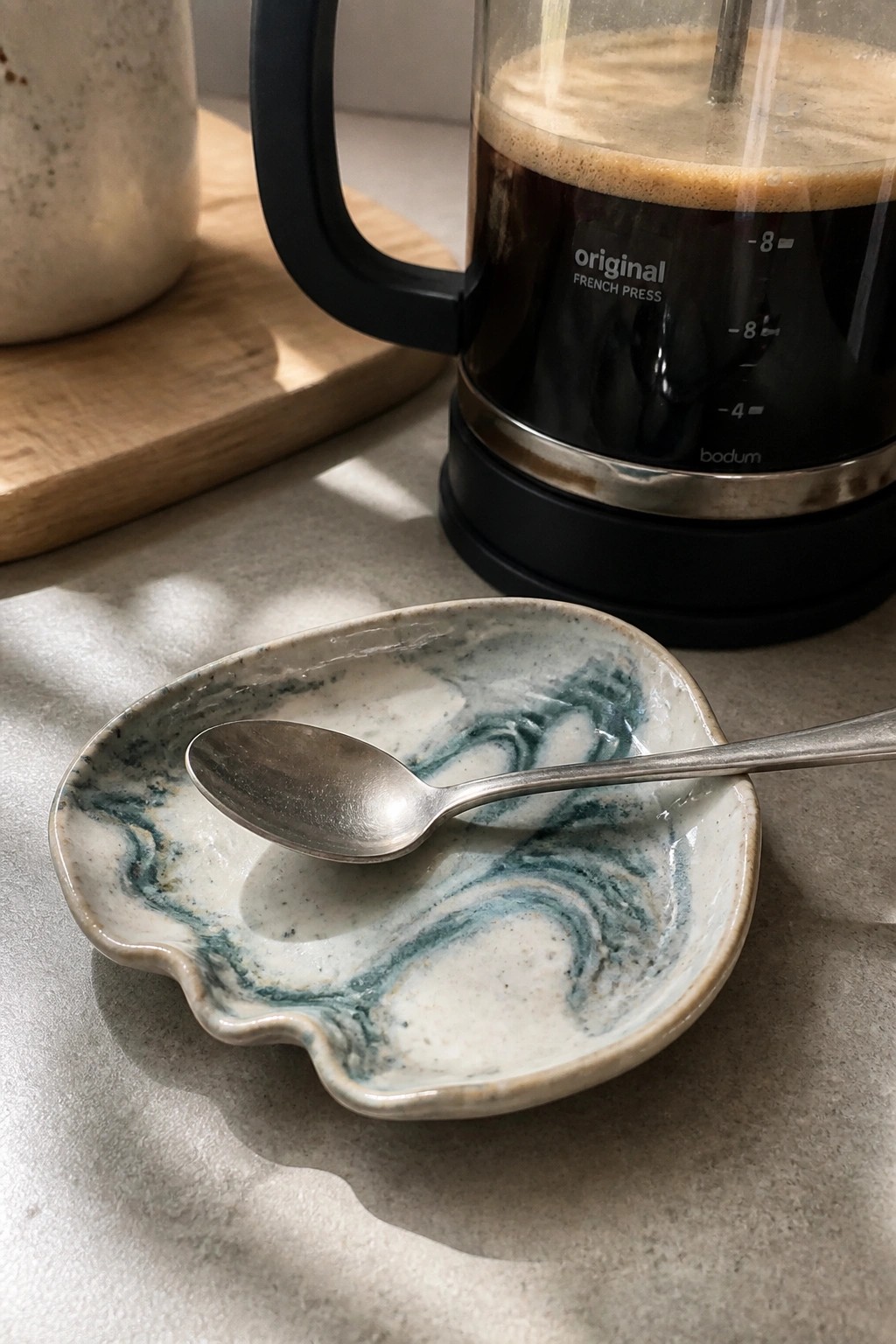 Stainless steel spoon in blue-white marbled ceramic dish beside Bodum French press