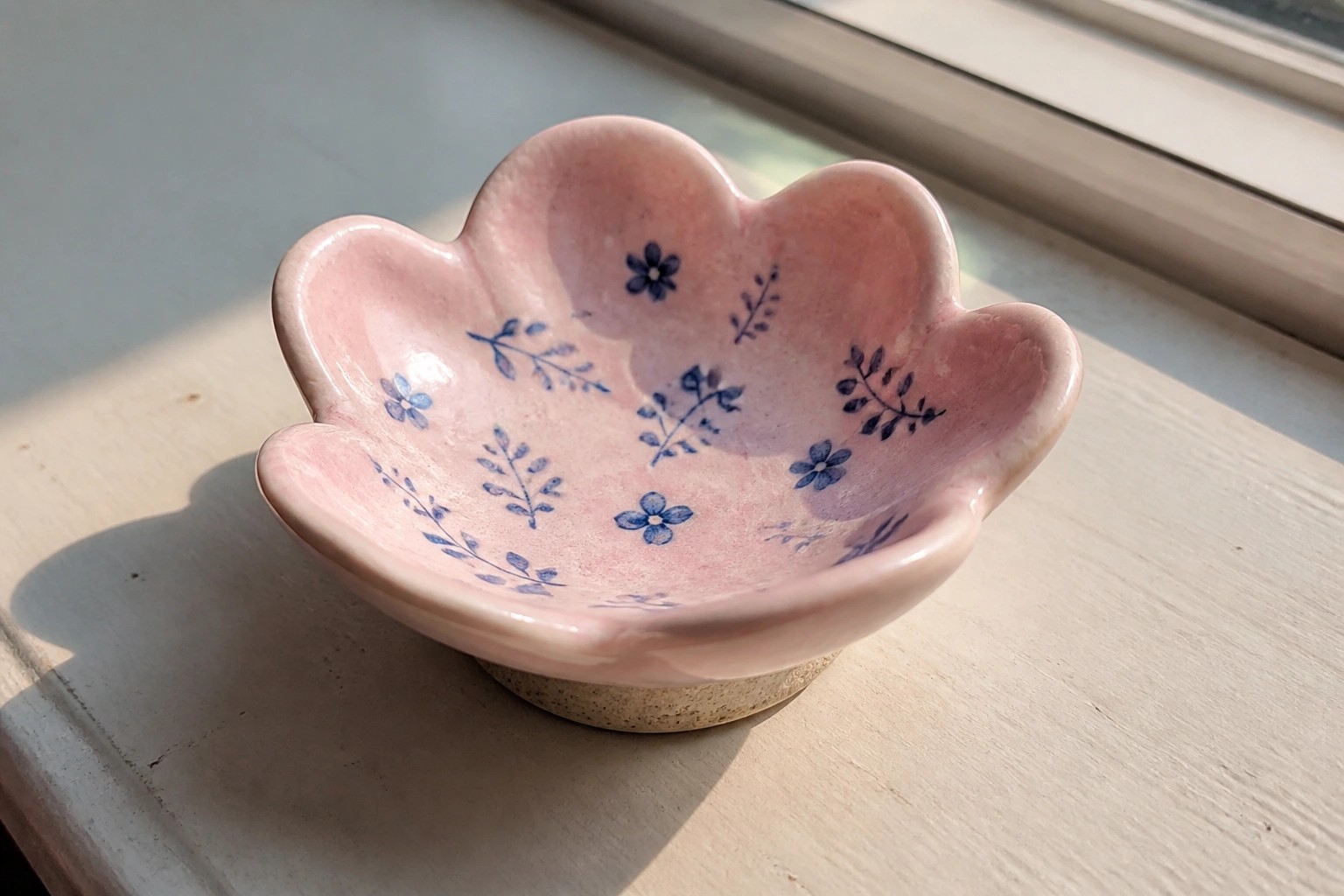 Pink flower-shaped ceramic bowl with blue floral patterns on white windowsill