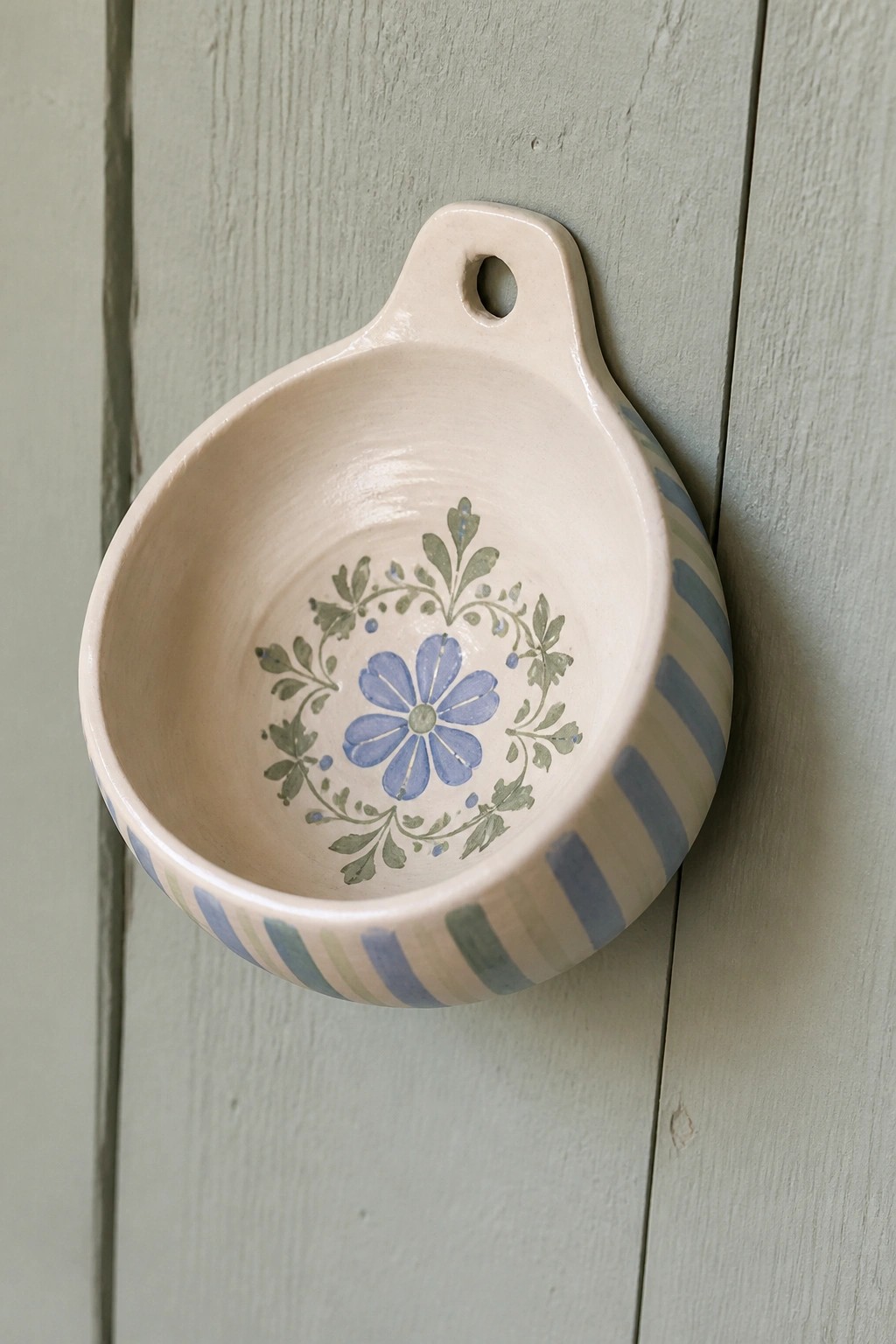 Ceramic bowl with blue flower and green leaves inside, blue stripes outside, on green wood.