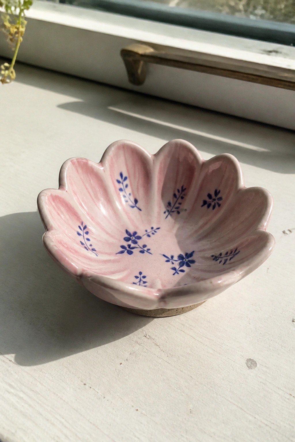 Pink flower-shaped ceramic bowl with blue floral patterns on white windowsill