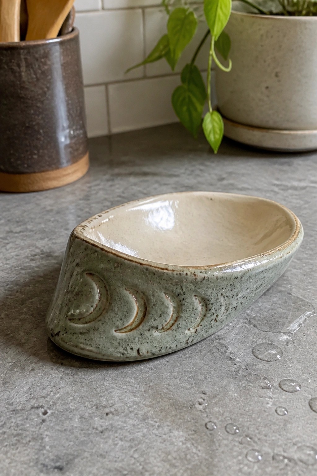 Green ceramic dish with moon phase carvings on wet gray countertop